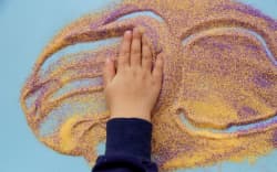 Baby hands plays with colorful sand. Child fine motor skills development. Creative kids occupation. View from above