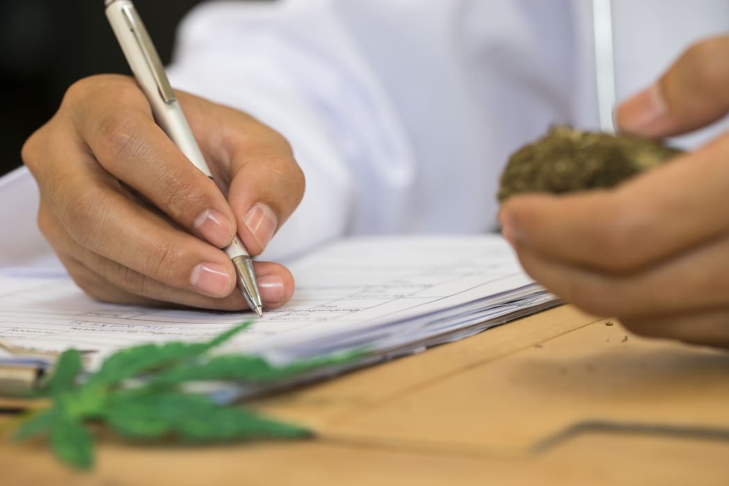 Doctor writing on prescription blank and bottle with medical cannabis on table close up