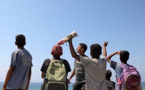 Children and youths gather as a C-130 Hercules military transport aircraft flies over during an aid drop on the northern Gaza Strip on 27 July, 2025.
