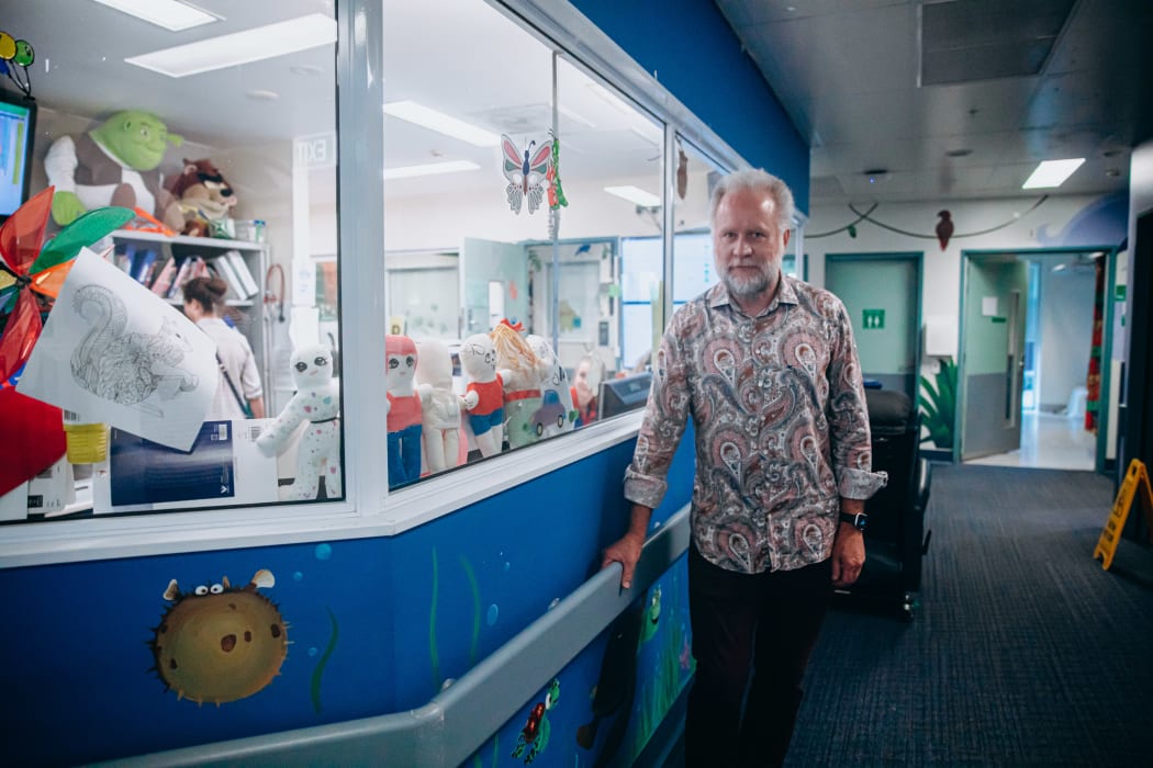 Man in paisely shirt stands new toys in a children's ward