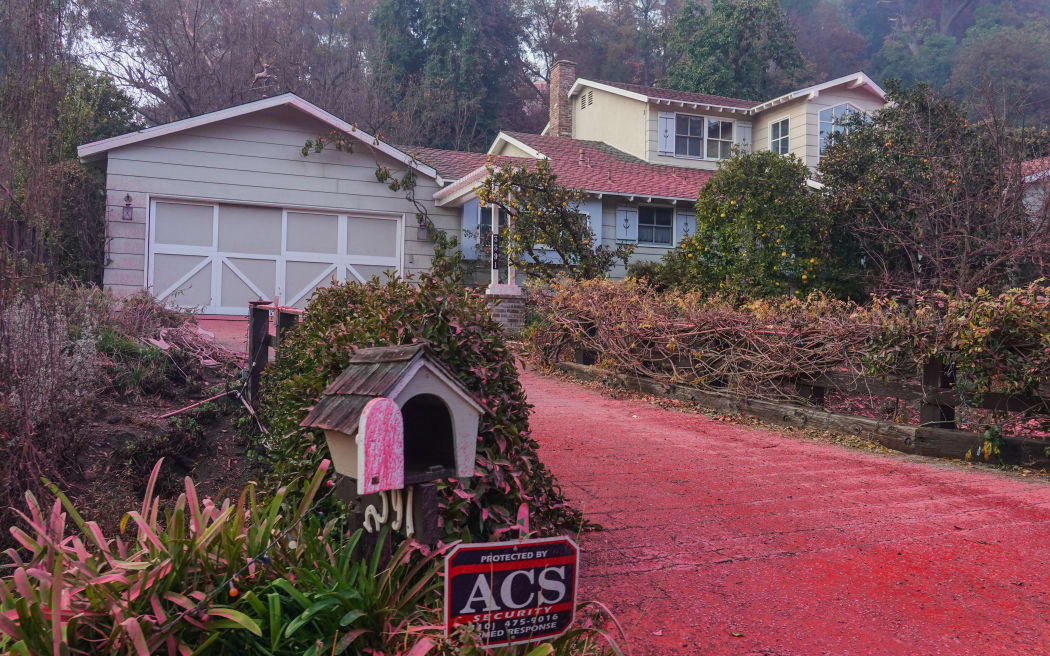 Foscheck fire retardant covers the road and nearby properties after being dropped by aircraft to slow the wildfire spread in Pacific Palisades, Los Angeles, California, on January 11, 2025, as wildfires continue in Los Angeles County. (Photo by Jason Ryan/NurPhoto) (Photo by Jason Ryan / NurPhoto / NurPhoto via AFP)
