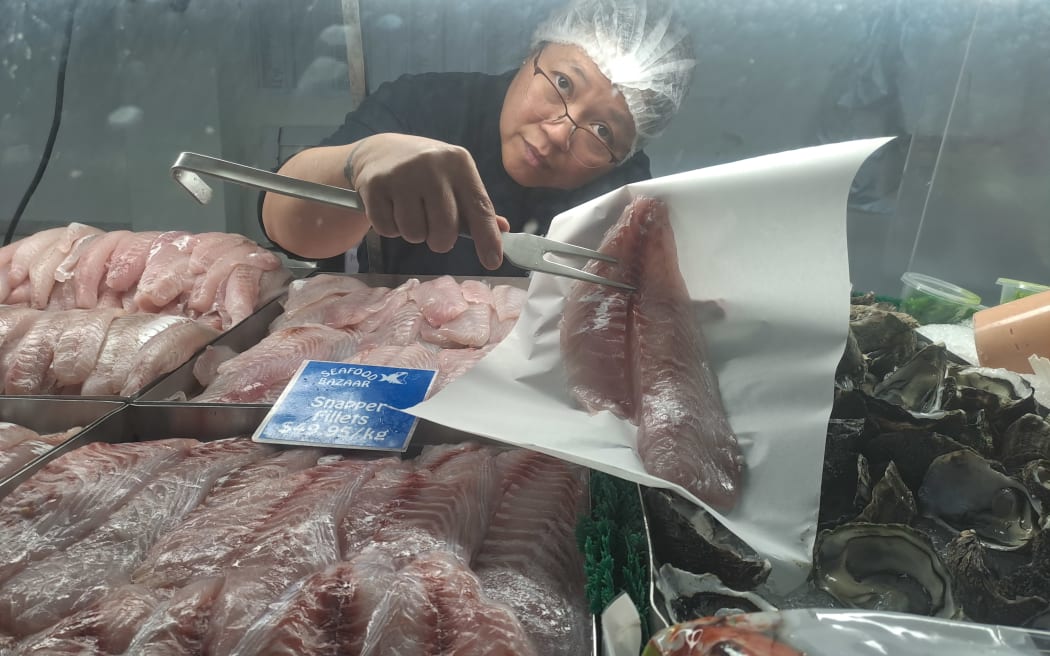 Seafood Bazaar staff member Cecilia Leonardo picks out snapper fillets for a customers