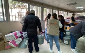 People stand holding supplies, including buckets and toilet paper in an aid shelter in Lebanon.