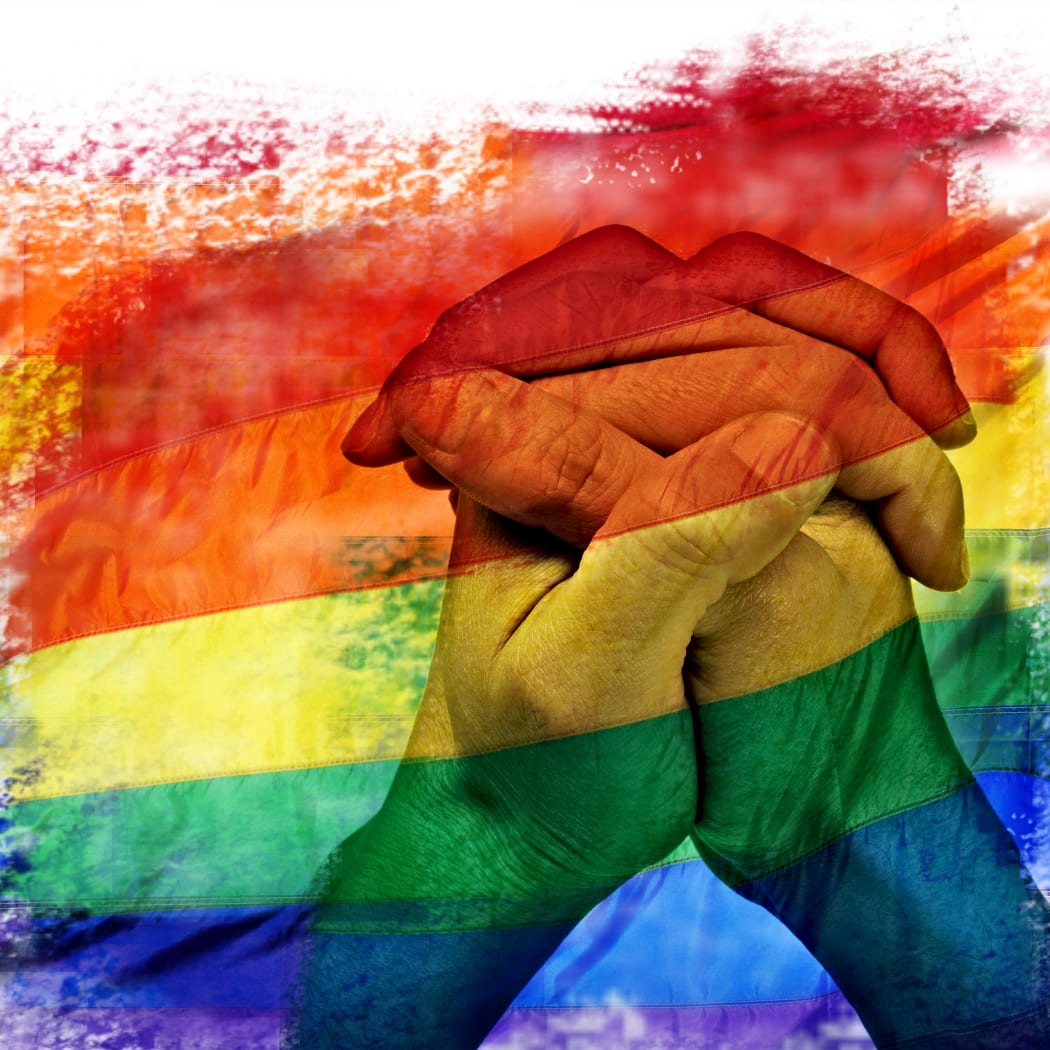 double exposure of a rainbow flag and the hands of a young man put together like praying