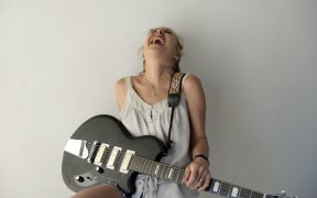 Kristin Hersh, laughing with her head back, holding a black electric guitar.