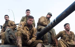 Brad Pitt and costars sit on top of a tank.