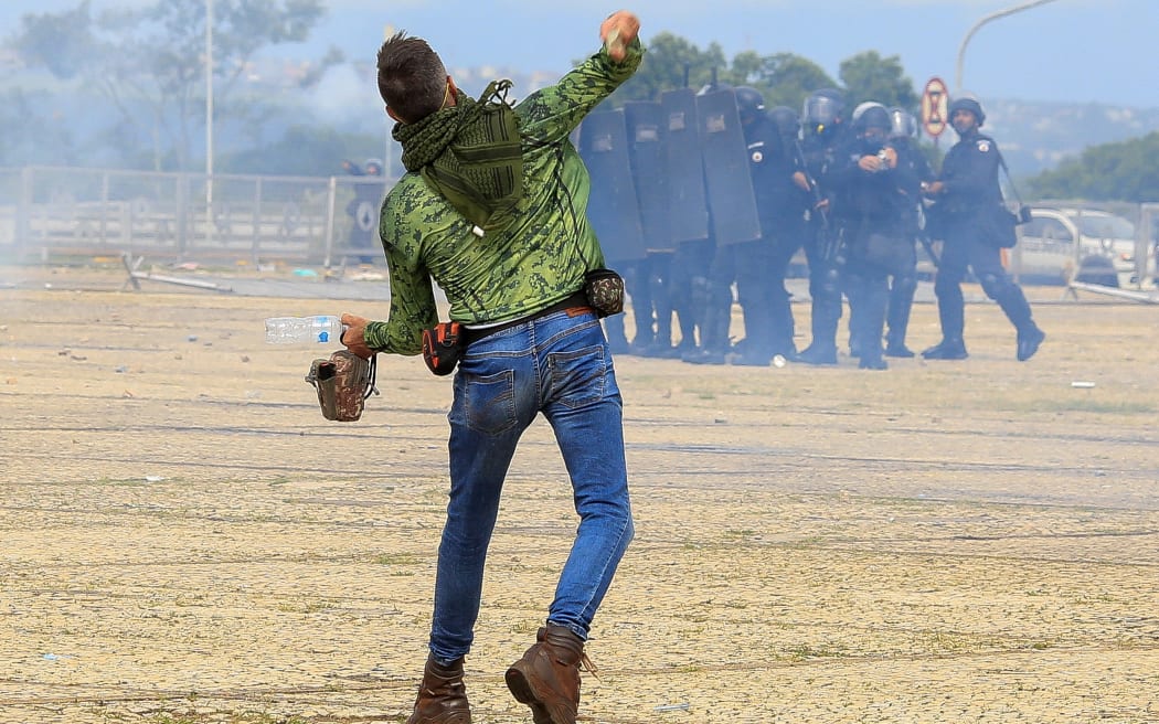 A supporter of Brazilian former President Jair Bolsonaro throws stones at security forces during clashes outside Planalto Presidential Palace in Brasilia on January 8, 2023. - Hundreds of supporters of Brazil's far-right ex-president Jair Bolsonaro broke through police barricades and stormed into Congress, the presidential palace and the Supreme Court Sunday, in a dramatic protest against President Luiz Inacio Lula da Silva's inauguration last week. (Photo by Sergio Lima / AFP)