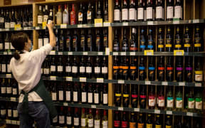 An employee works as Australian-made wine (on display shelves on R) are seen for sale at a store in Beijing on August 18, 2020. -