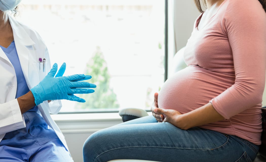 An unrecognizable female doctor wears protective mask and gloves as she prepares to examine an unrecognizable pregnant woman.