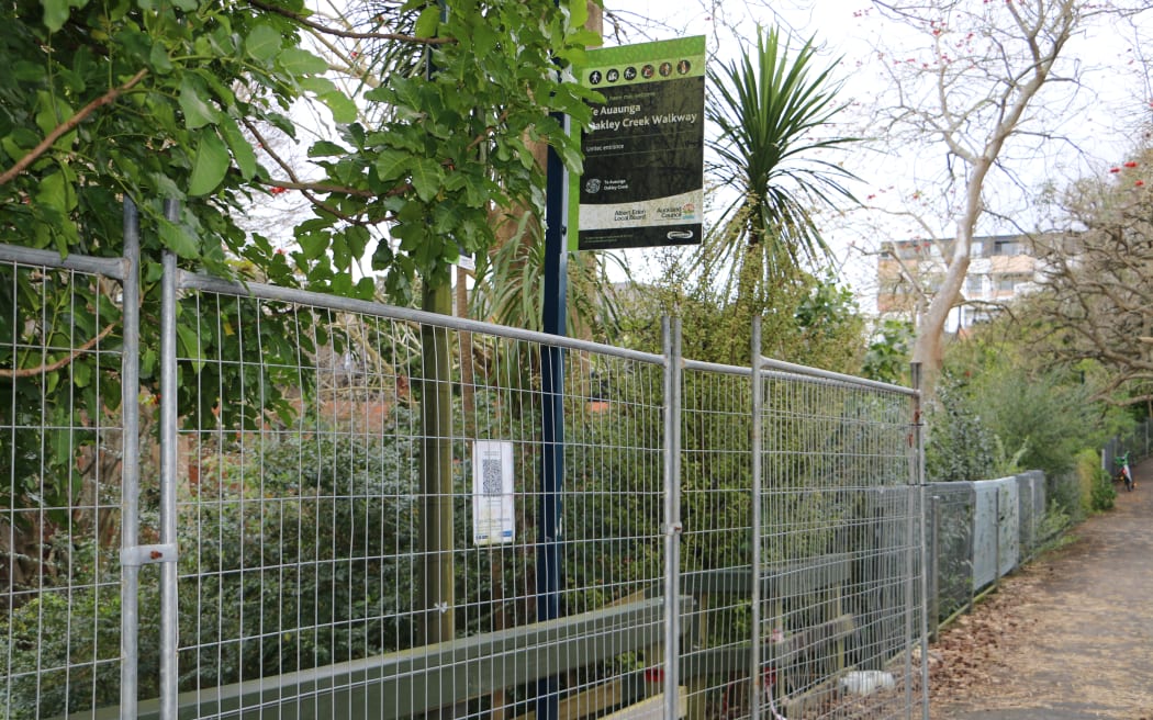 A sign for the Oakley Creek walkway, with a fence in front of it.