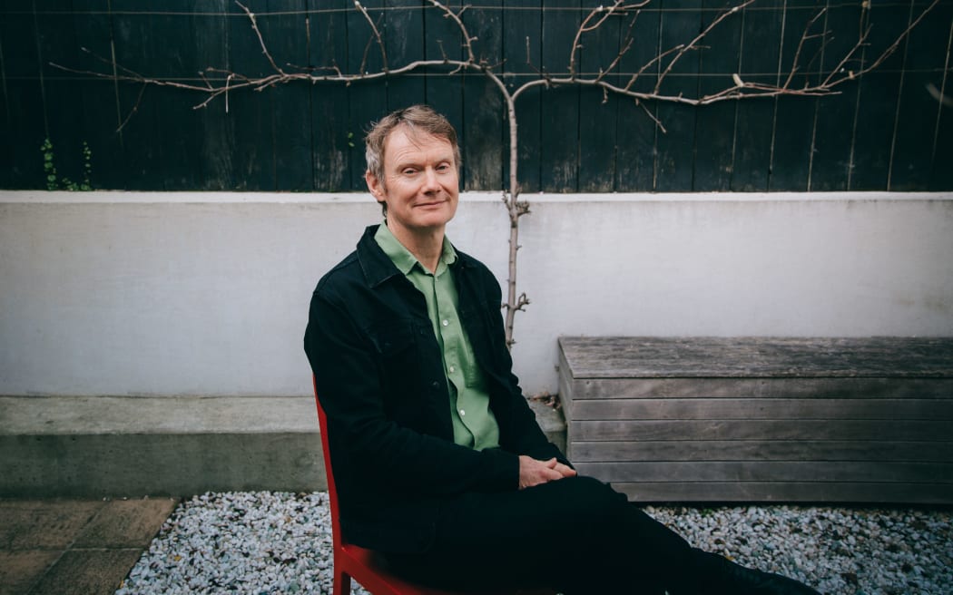 Wellington professor and author Damien Wilkins sitting in a chair in a courtyard.