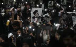 Mourners hold up a posters of the late Iranian President Ebrahim Raisi at the mam Khomeini Grand Mosque in Tehran, Iran, Tuesday, May 21, 2024 during a funeral ceremony for him and his companions who were killed in a helicopter crash on Sunday in a mountainous region of the country's northwest. Mourners in black began gathering Tuesday for days of funerals and processions for Iran's late president, foreign minister and others killed in a helicopter crash, a government-led series of ceremonies aimed at both honoring the dead and projecting strength in an unsettled Middle East. (AP Photo/Vahid Salemi)