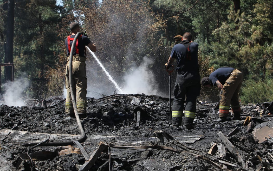 Firefighters pour water on cinders during a response effort to a Russian drone attack in a suburb of Dnipro, Ukraine,