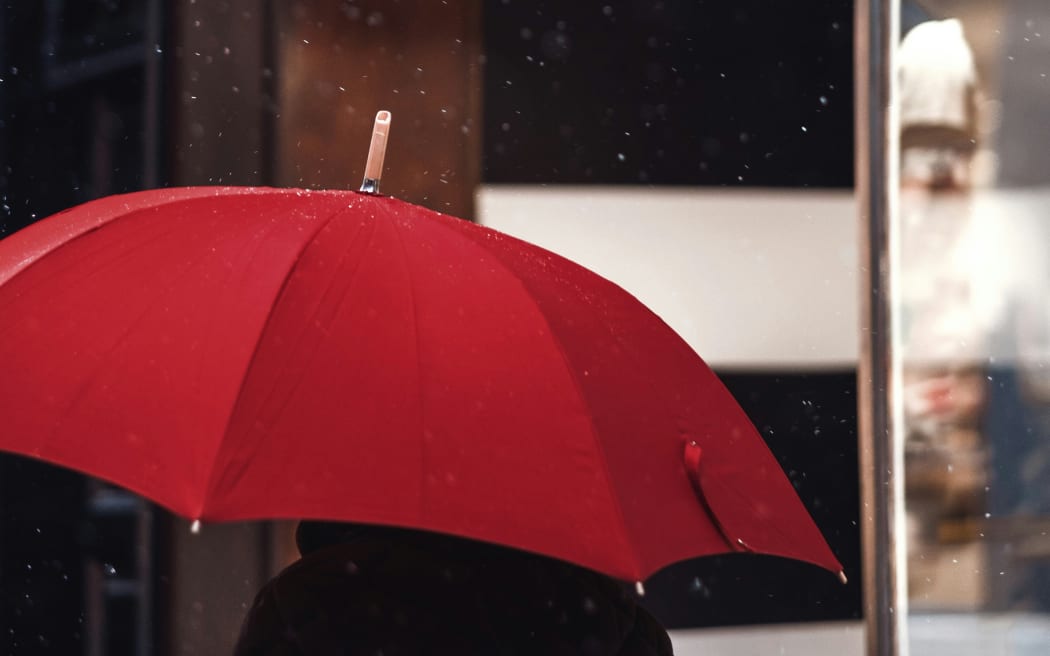 A person walks with a red umbrella on a rainy day.