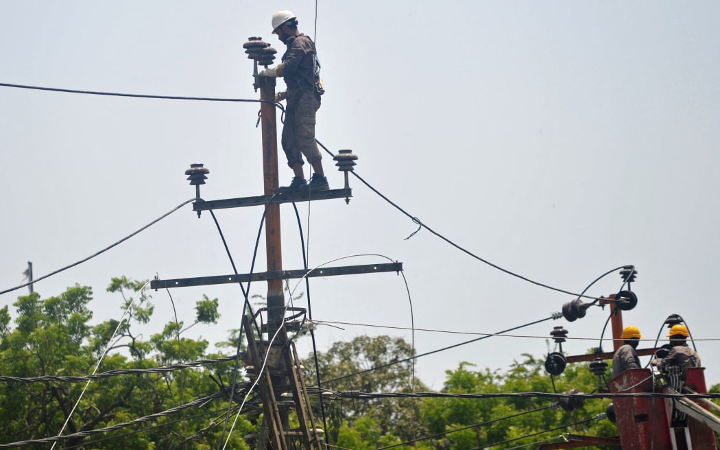 Men work on electric pylons along the roadside in Karachi on 30 May 30, 2021.