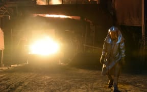A steelworker in a protective suit checks the temperature of molten metal in furnace at a plant Pennsylvania.