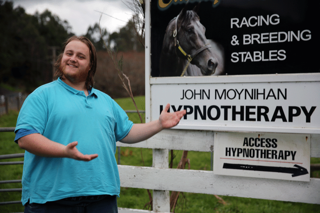 A picture of Uther Dean standing in front of a sign that identifies a horse breeder and a hypnotist