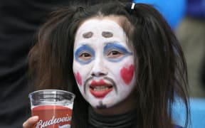 A Japan fan with a painted face enjoys a  beer.