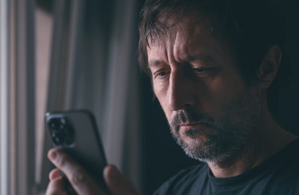 Man reading text message on mobile phone while standing by the apartment window, selective focus