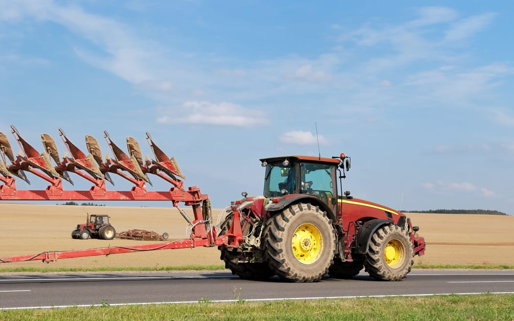 two tractors with  ploughs - one on the road, another - in field