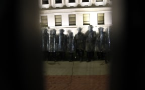 Police in riot gear are seen through the iron fence protecting the County Courthouse during demonstrations against the shooting of Jacob Blake