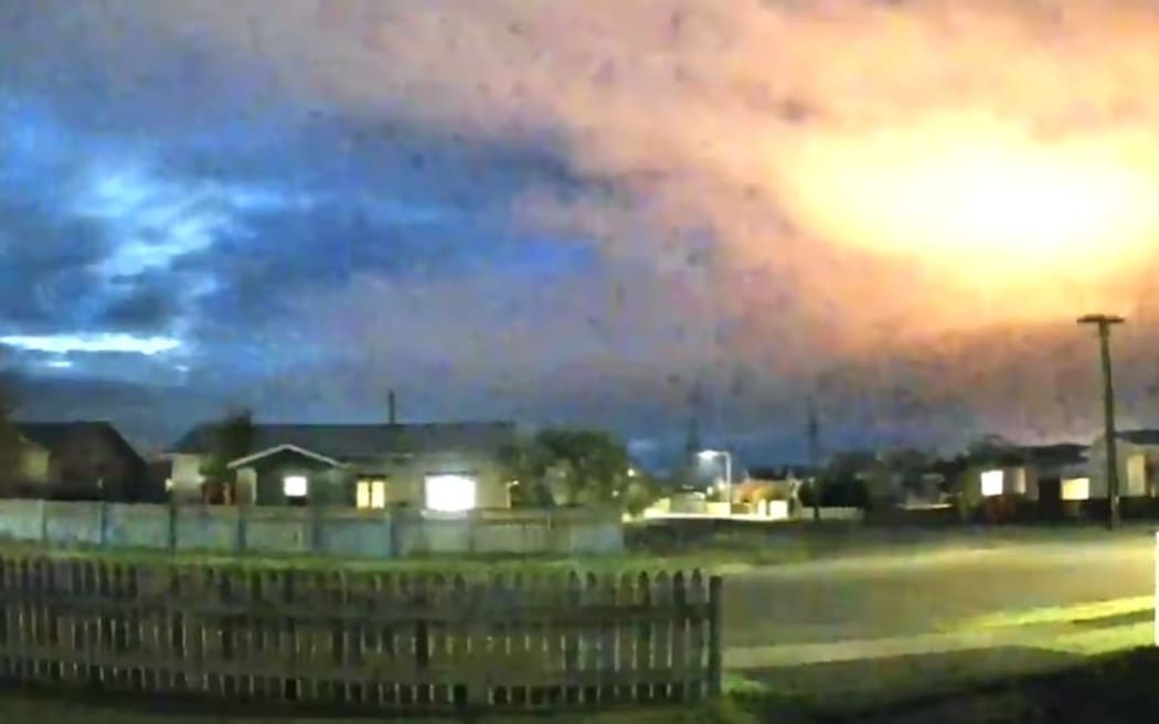 A residential street with a very bright light in the sky in the right hand corner.