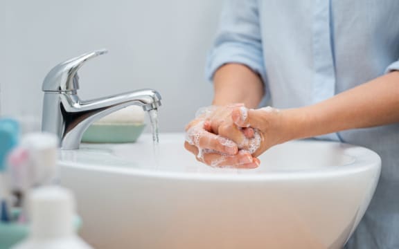Closeup of woman applying soap while washing hands in basin with open tap. Mature woman washing hands for cleanliness purpose. Lady rubbing hands filled with soap.
