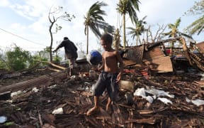 A young boy kicking a ball as his father searches through the ruins of their family home in Vanuatu's capital Port Villa after Cyclone Pam ripped through the island nation.