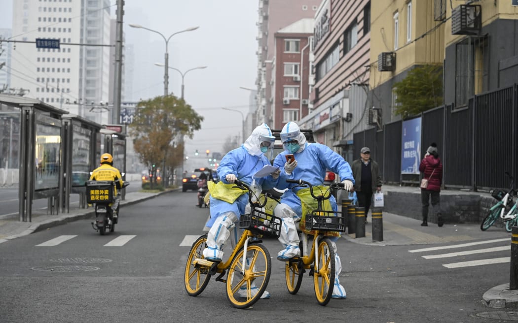 Health workers in personal protective equipment (PPE) carrying Covid-19 coronavirus testing swabs and tubes are seen on bicycles on a Beijing street, 24 November, 2022.