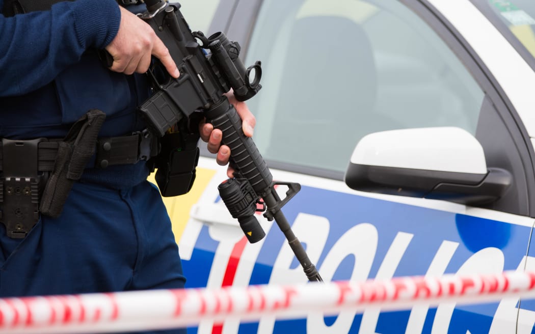 A police officer stands watch at the edge of a cordon of a crime scene holding a gun