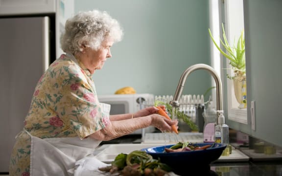 An elderly woman prepares food in her kitchen.