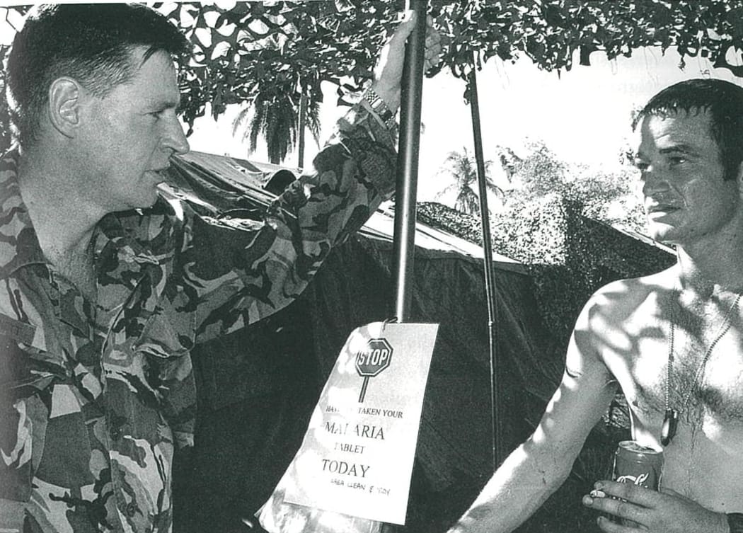 : Lieutenant Colonel Kevin Burnett (at left) talking to one of his men. The sign in the middle of the photograph reminds personnel to take their daily doxycycline tablet to guard against malaria.