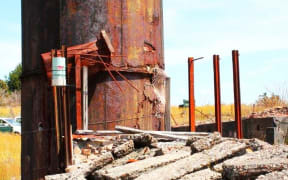 A rusty orange condensing tower at New Zealand's most toxic site, the historic Prohibition gold mine at Waiuta on the West Coast.  Surround but rusty metal and large lumps of broken concrete