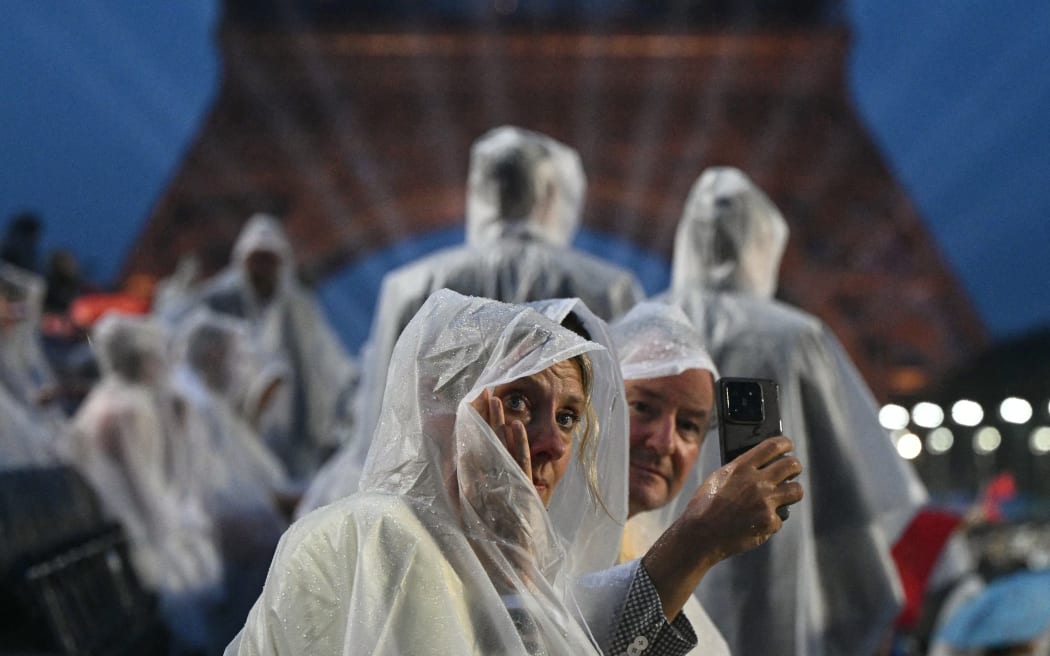 Attendees wear rain covers as they sit in the stands during the opening ceremony of the Paris 2024 Olympic Games in Paris on July 26, 2024, with the Eiffel Tower in the background.