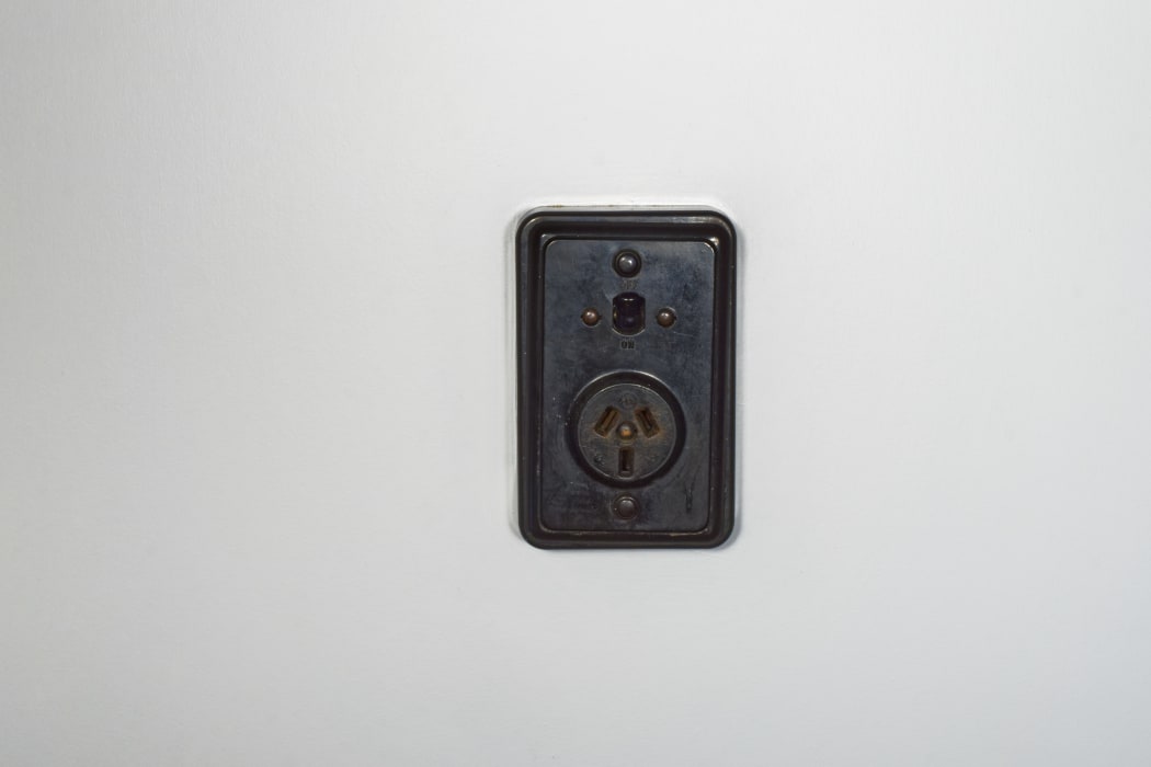 Old fashioned bakelite power socket with on/off switch on a white plaster wall