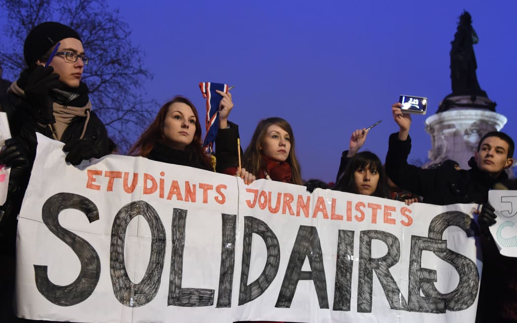Journalism students hold a banner reading in French: "Journalism students : Solidarity" as they raise pens during a gathering at the Place de la Republique.