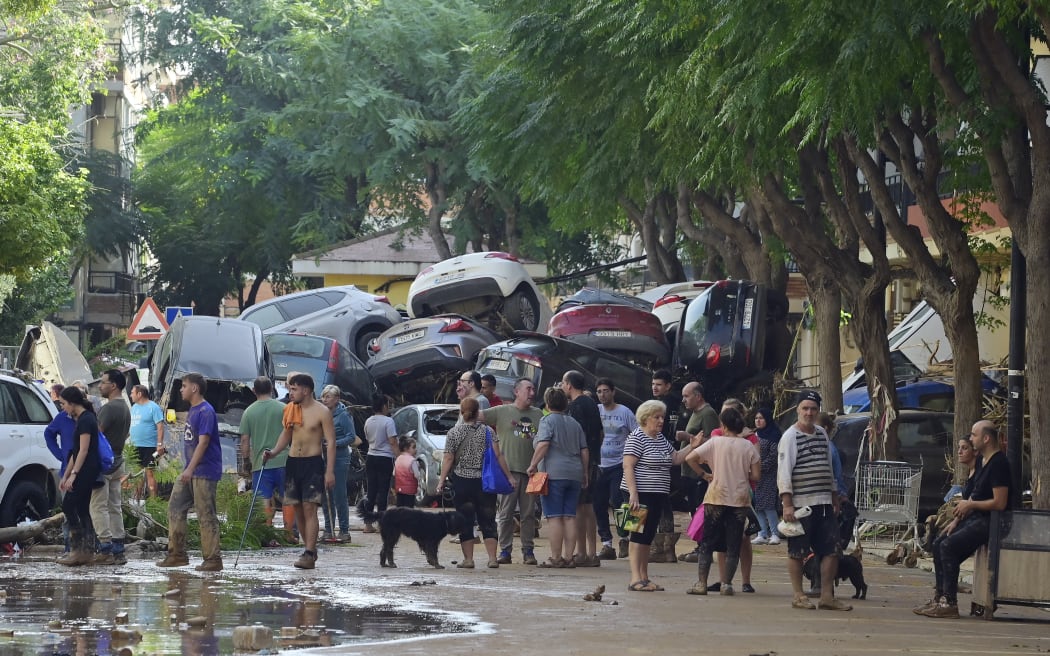 Residents gather in the street next to a pile of cars on October 31, 2024 after flash floods affected the town of Massanassa, in the region of Valencia, eastern Spain. - Rescuers raced on October 31, 2024 to find survivors and victims of once-in-a-generation floods in Spain that killed at least 95 people and left towns submerged in a muddy deluge with overturned cars scattered in the streets. About 1,000 troops joined police and firefighters in the grim search for bodies in the Valencia region as Spain started three days of mourning. Up to a year's rain fell in a few hours on the eastern city of Valencia and surrounding region on October 29 sending torrents of water and mud through towns and cities. (Photo by JOSE JORDAN / AFP)