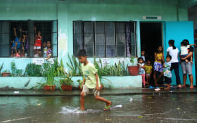 A young evacuee wades through flooded school grounds while others look on from a school building being used as an evacuation center in the city of Legaspi in Albay province, south of Manila on December 14, 2015,