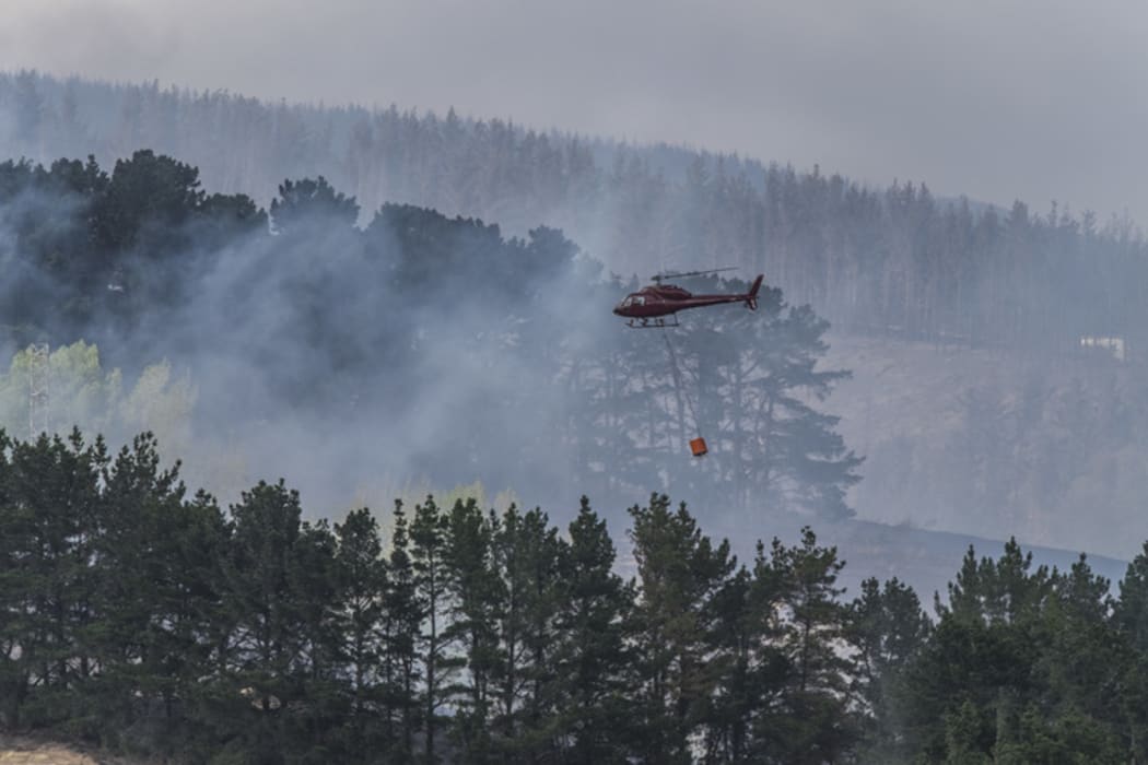 A helicopter flies in a load of water in a monsoon bucket during fire fighting efforts in the Port Hills.