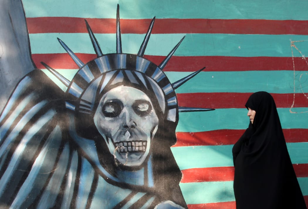 A woman in Tehran walks past a mural on the wall of the former US embassy.