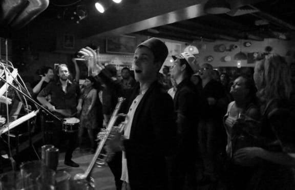 The band features violins, trombones, trumpets, bouzoukis, accordion, clarinet, drums, saxophone and guitar.