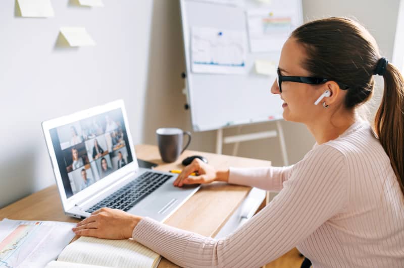 Morning meeting online. A young woman is using app on laptop for connection with colleagues, employees. Video call with many people together. Back view