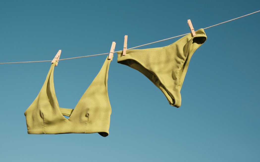 A green bikini pegged on a washing line against a blue sky.