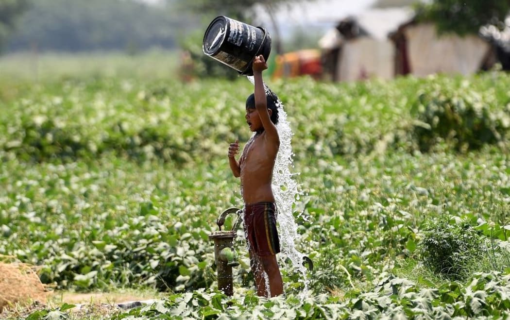 (FILES) In this file photo taken on May 29, 2019, an Indian boy pours water on himself as he tries to cool himself off amid rising temperatures in New Delhi. -