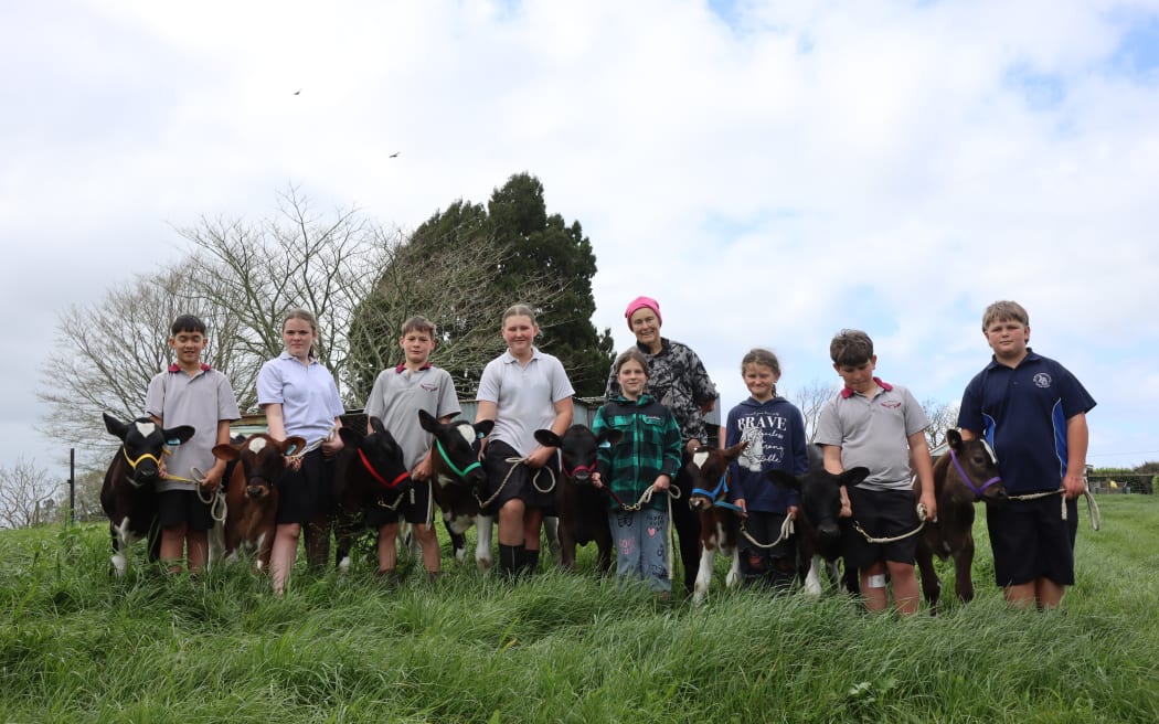 A group photo of eight children posing with their calves, and Janet Macky standing behind them.