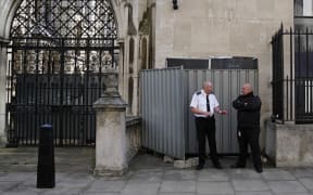 Security guards stand beside a metal barrier covering up an artwork by street artist Banksy, depicting a judge using a gavel to beat a protester using a placard as protection, on an exterior wall of the Royal Courts of Justice in London, on September 8, 2025. (Photo by CARLOS JASSO / AFP)