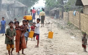 Children stand in mud and rock road carrying yellow plastic containers