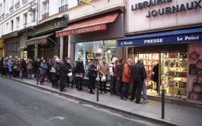 People wait outside a newsagents in Paris as the latest edition of French satirical magazine Charlie Hebdo goes on sale.