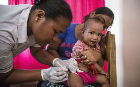 Taratiteiti Kirition holding her 1-year-old daughter Pepeeti while a nurse gives her an immunisation shot at a Kiribati clinic