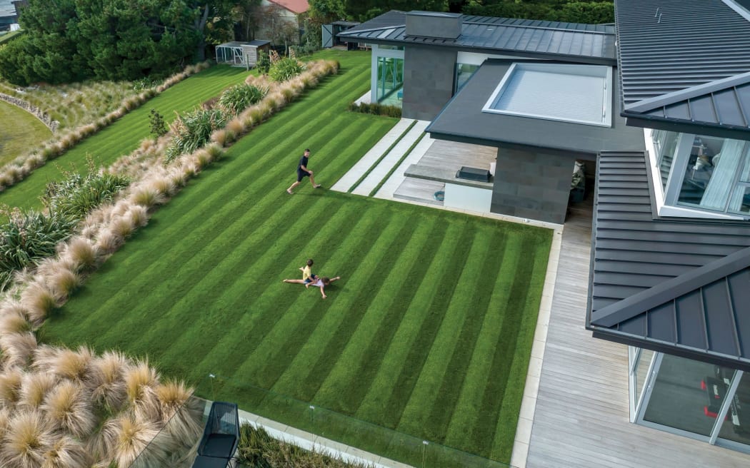 A perfectly striped lawn next to a grey and glass house. Children play on the lawn.